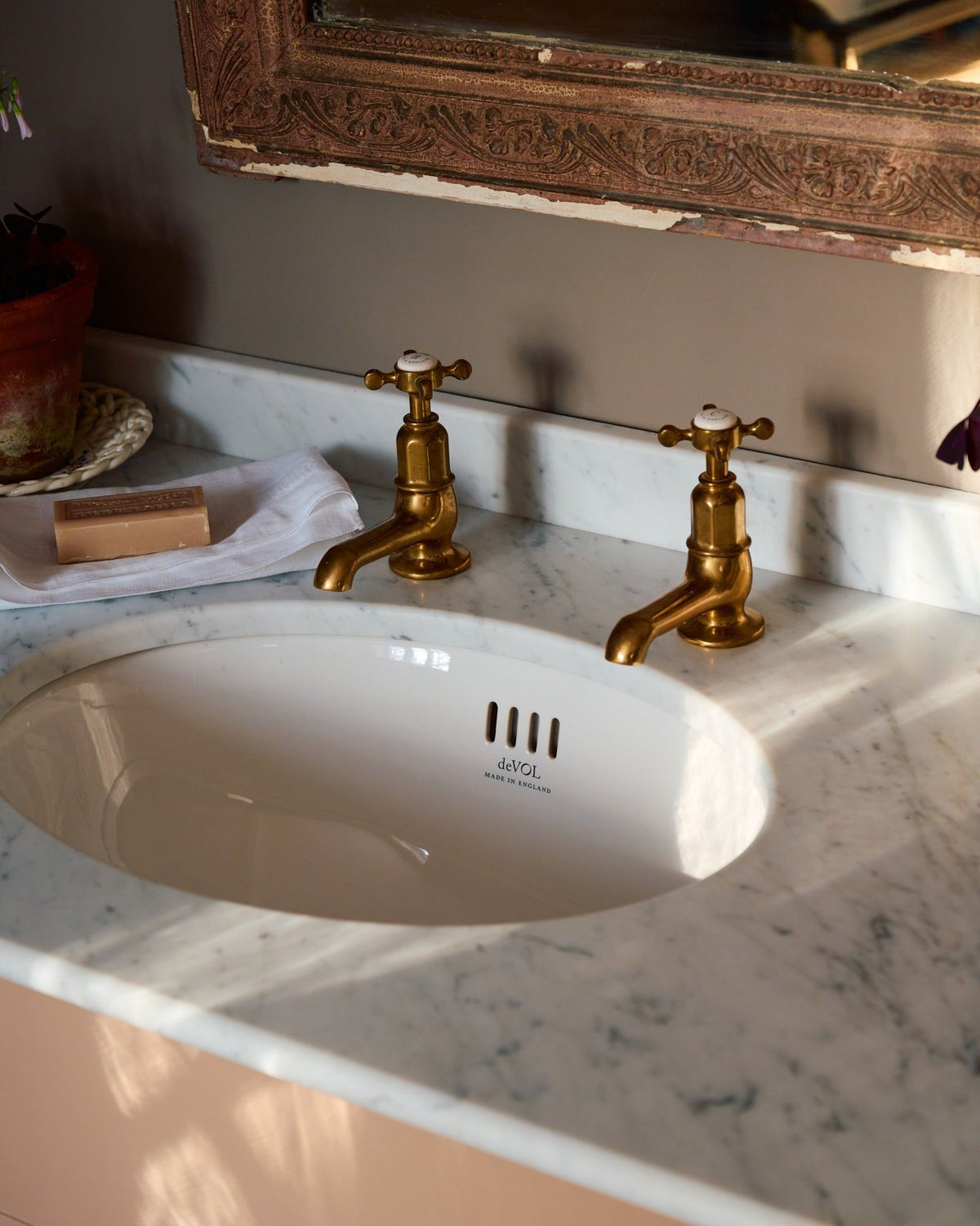 An oblique view of a pair of aged brass pillar taps with crosshead handles for a bathroom basin sink. TEST