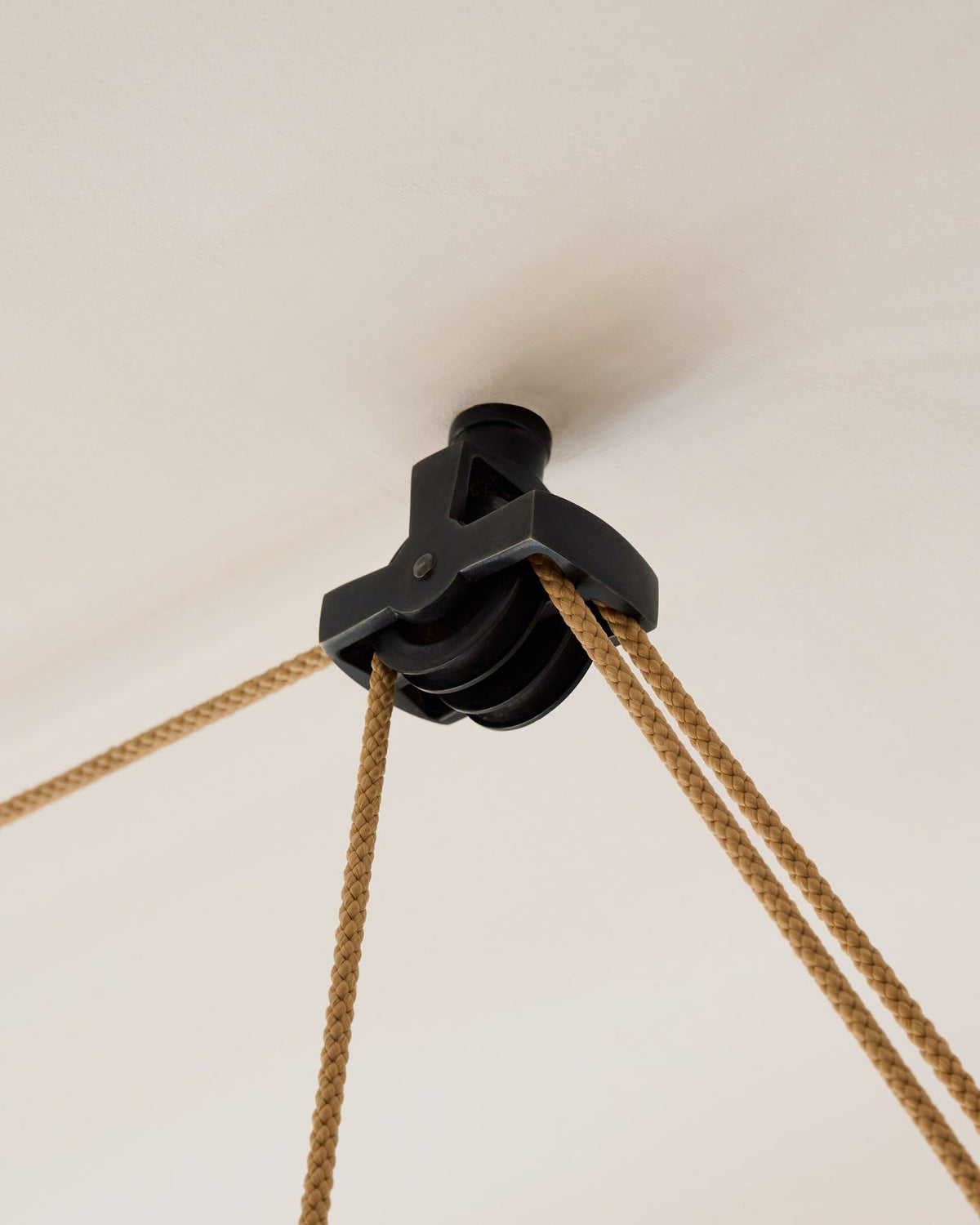 A close-up view of a black brass wheel pulley fixed to a white ceiling. TEST