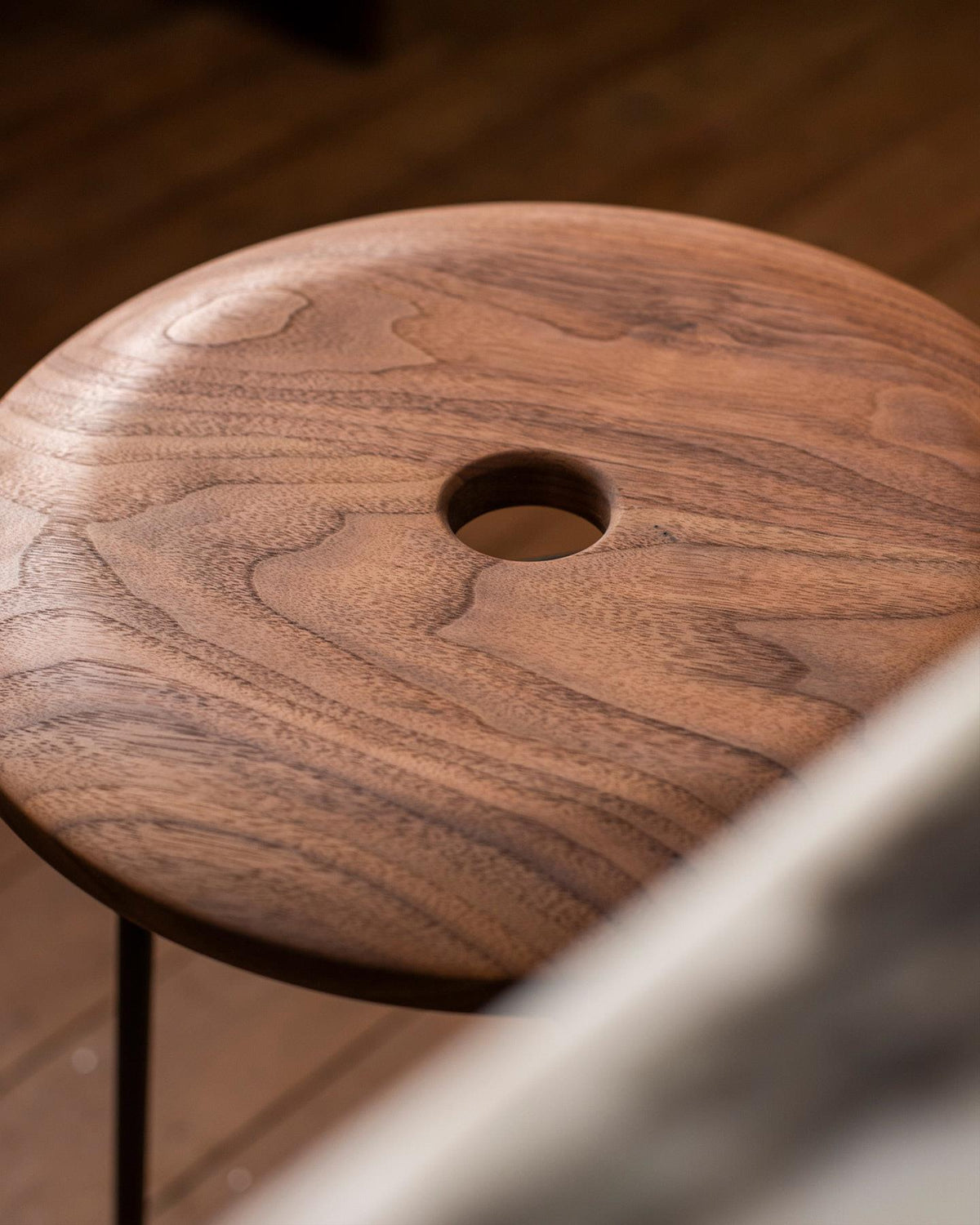 A close-up view of a round walnut seat top with a central hole and a natural oiled finish. TEST
