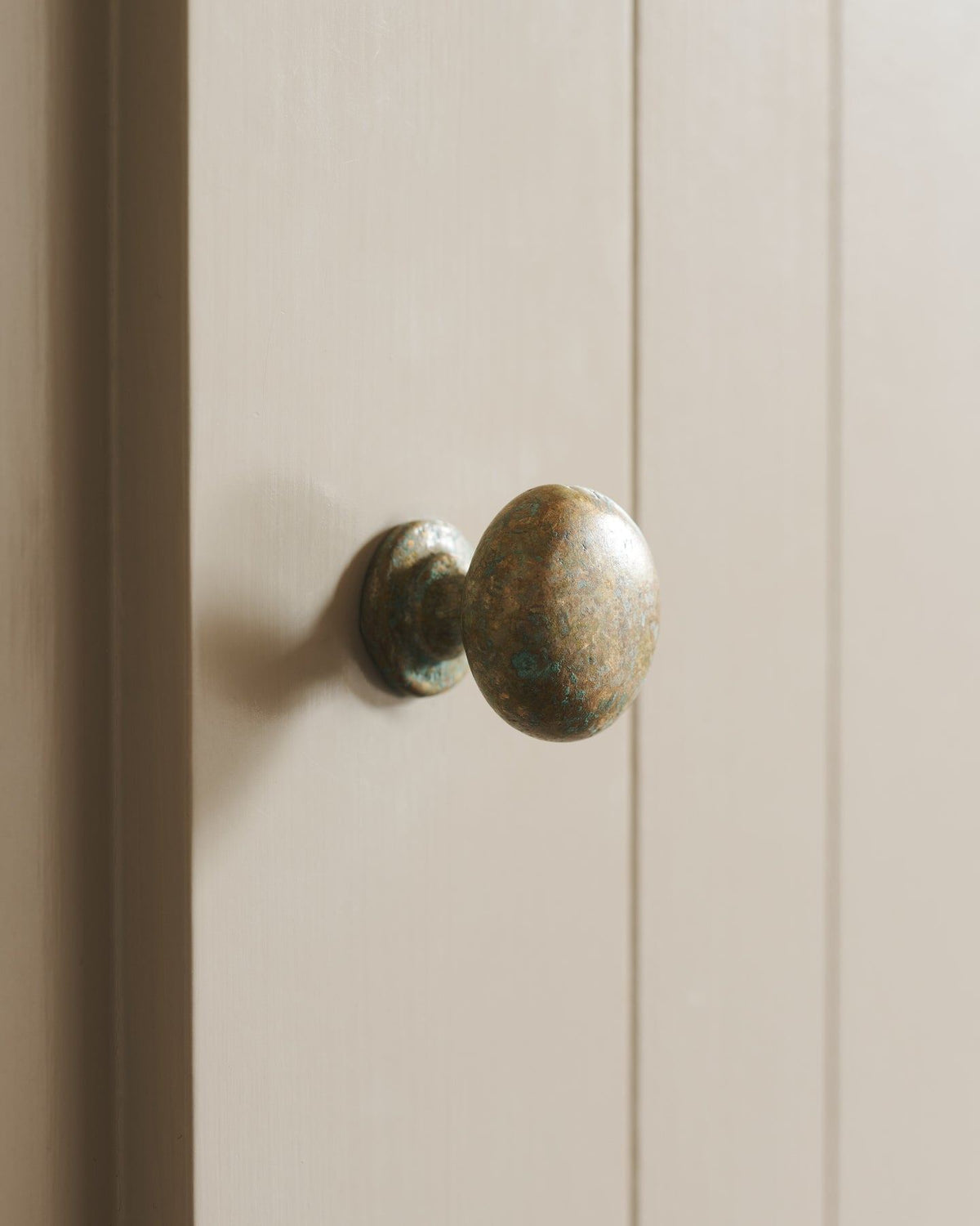 A close-up oblique view of a classic knob in an aged verdrigris brass finish, fitted to a mushroom painted cupboard door.|Medium shown TEST