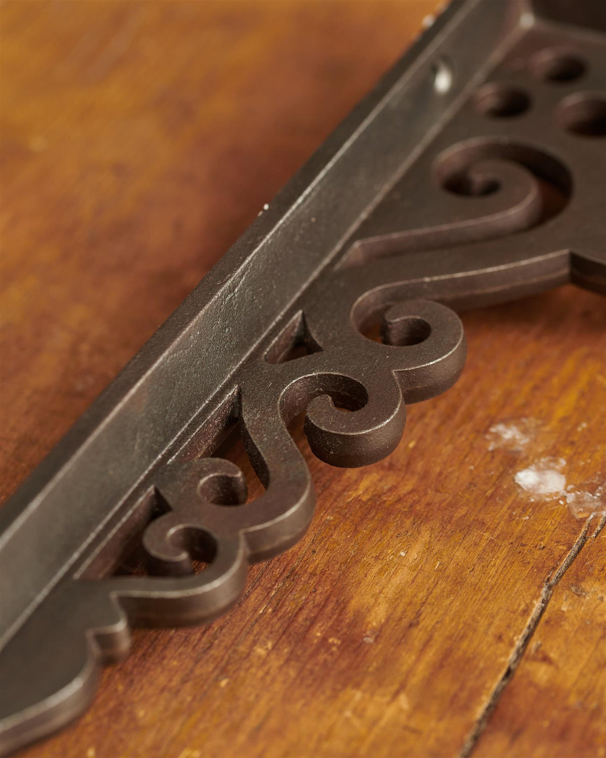 A close-up view of the decorative cutout patterns on a large Victorian-inspired ornate cast iron shelf bracket. TEST
