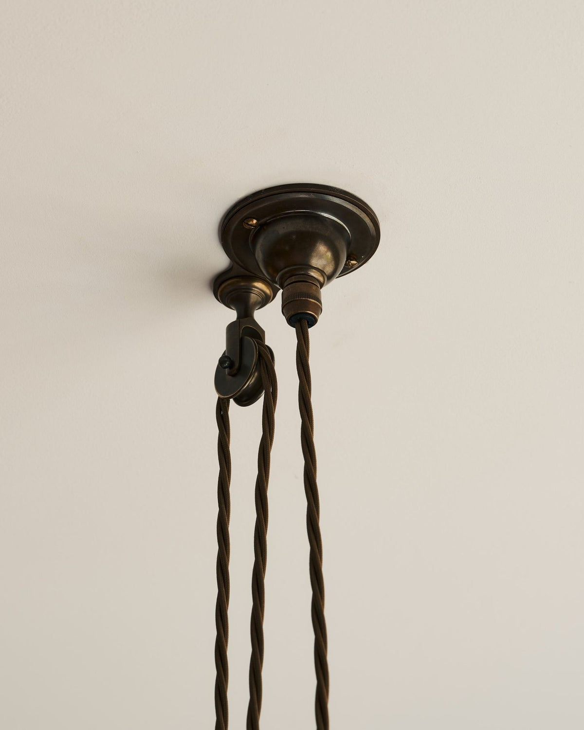 A small aged brass ceiling rose with a wheel pulley and a brown twisted fabric flex cord. TEST