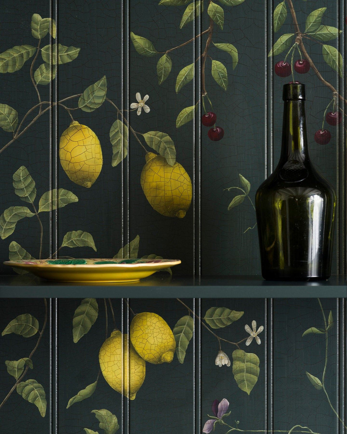 A close-up view of a dark green painted cupboard interior with hand-painted botanical flora, lemons and cherries on a tongue and groove-style backboard. TEST