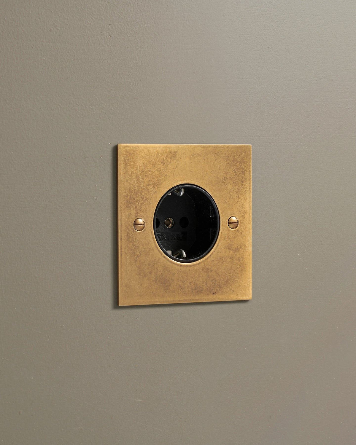 An oblique view of a classic Schuko-style single plug socket in a mottled aged brass finish. TEST