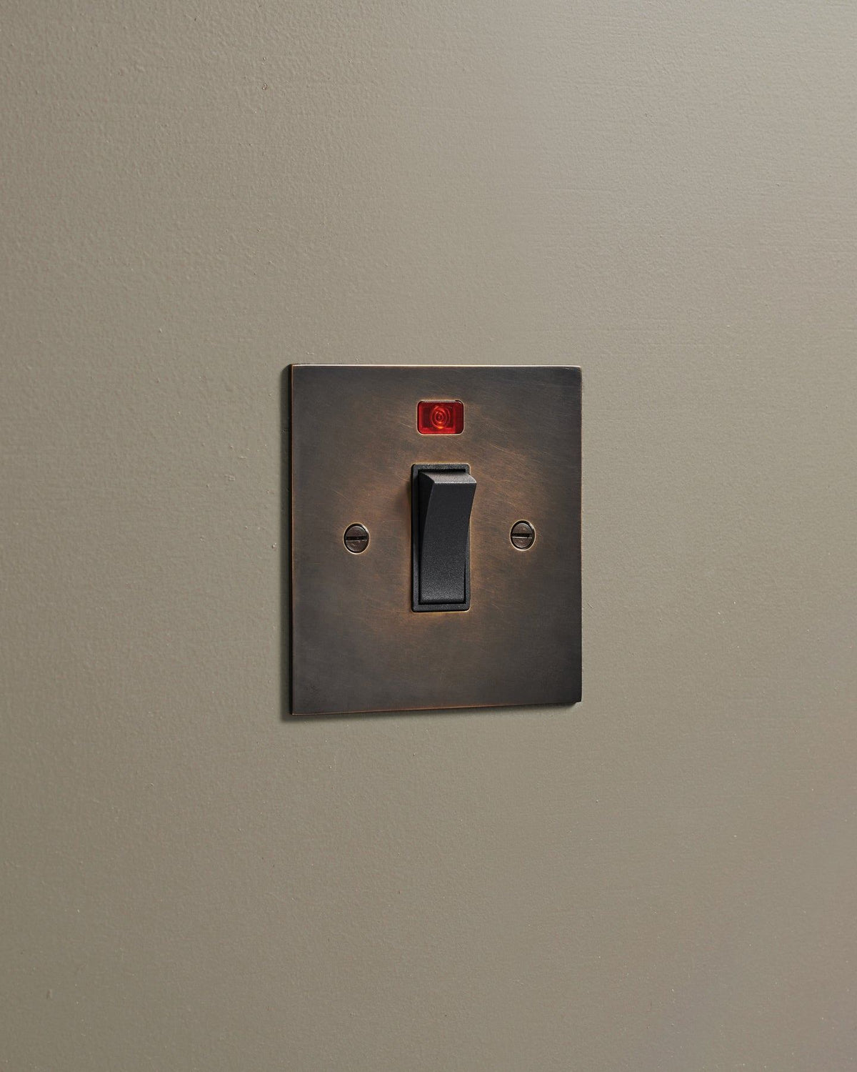 An oblique view of a classic 32 amp cooker switch in a dark oxidised brass finish. TEST