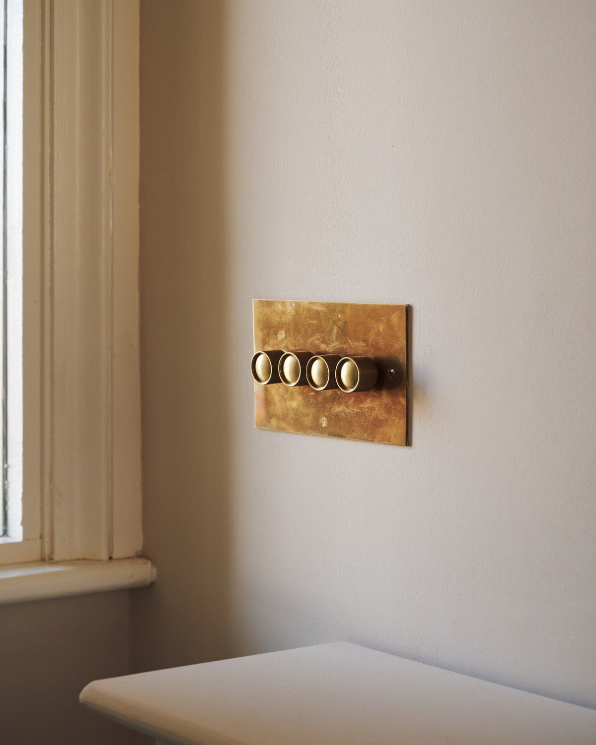 An oblique view of a 4 gang classic dimmer switch in a warm burnished brass finish on soft pink walls with light painted woodwork. | Heirloom Brass 4 Gang shown TEST