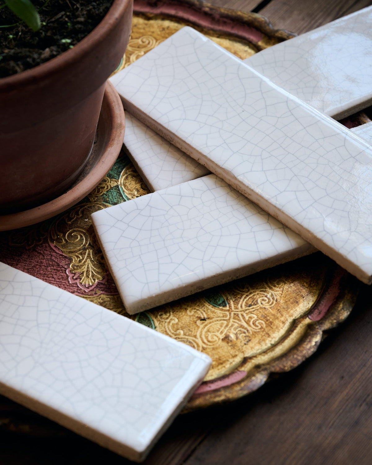 Several white glossy metro tiles on a decorative brass plate, each tile has unique delicate crazing across the surface. TEST
