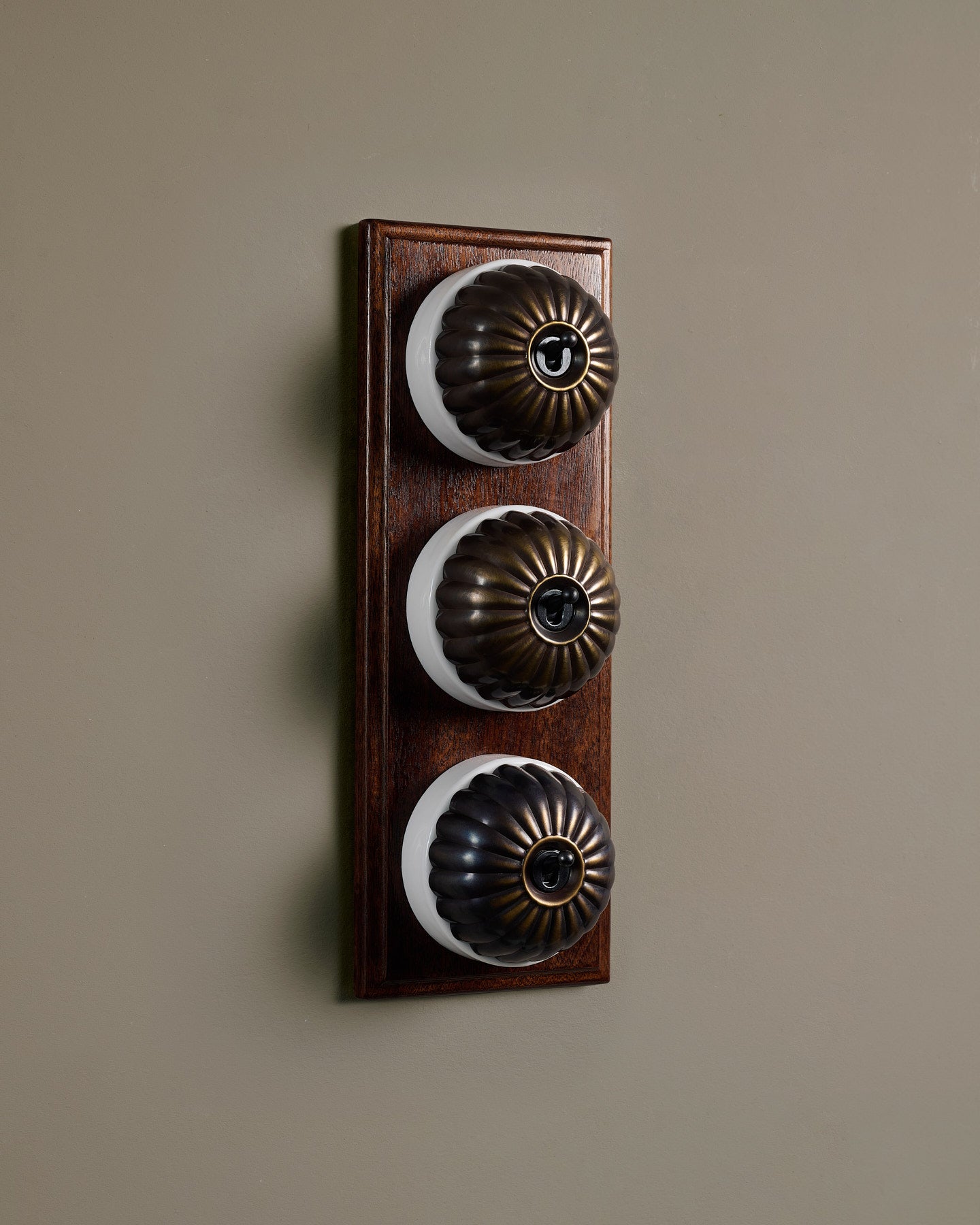 The Jelly Toggle Switch (3 Gang & Mahogany Finish Pattress) - Oxidised Brass with White Base.