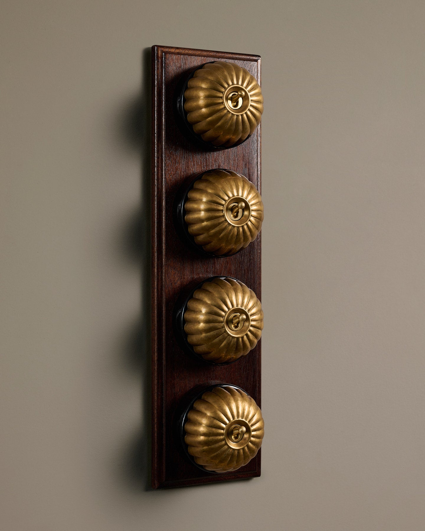 The Jelly Toggle Switch (4 Gang Row & Mahogany Finish Pattress) - Aged Brass with Black Base.