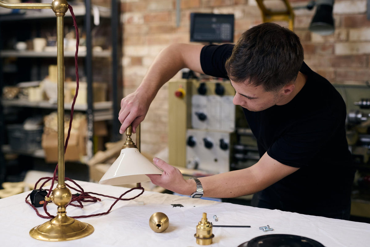 A product designer putting together the wires inside the brass pieces of the grand tour library lamp.