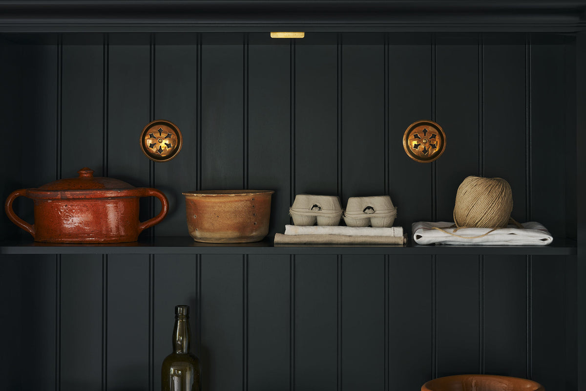 A close-up look inside a pantry cupboard are a pair of brass ventilation grille.