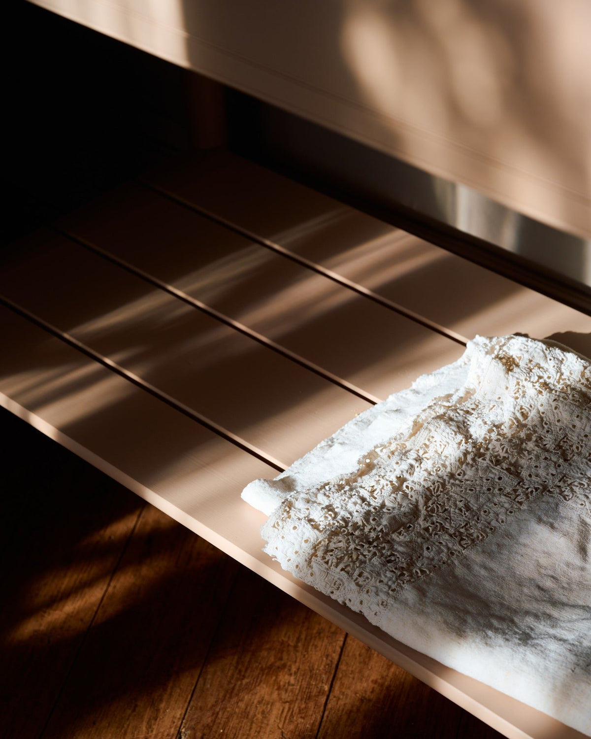 A close-up view of a pink painted slatted shelf at the base of a Victorian-inspired washstand. TEST
