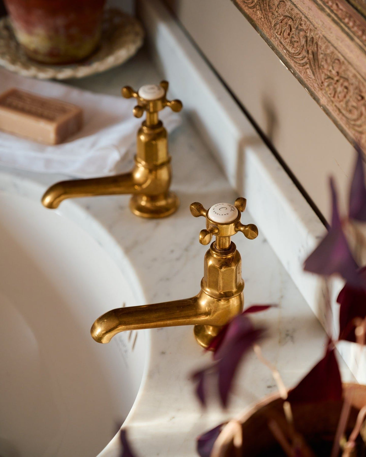 An oblique view of a pair of aged brass pillar taps with crosshead handles for a bathroom basin sink. TEST