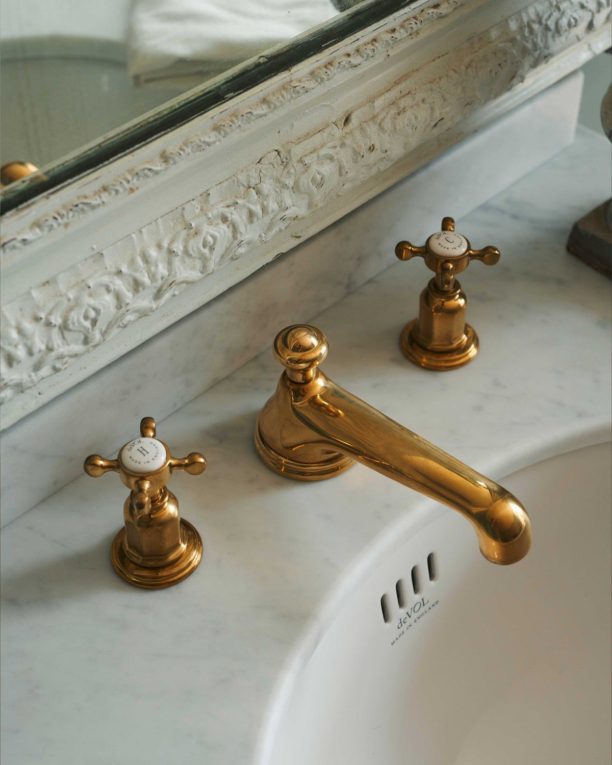 Gold bathroom faucet and handles on a marble sink with decorative mirror above. TEST