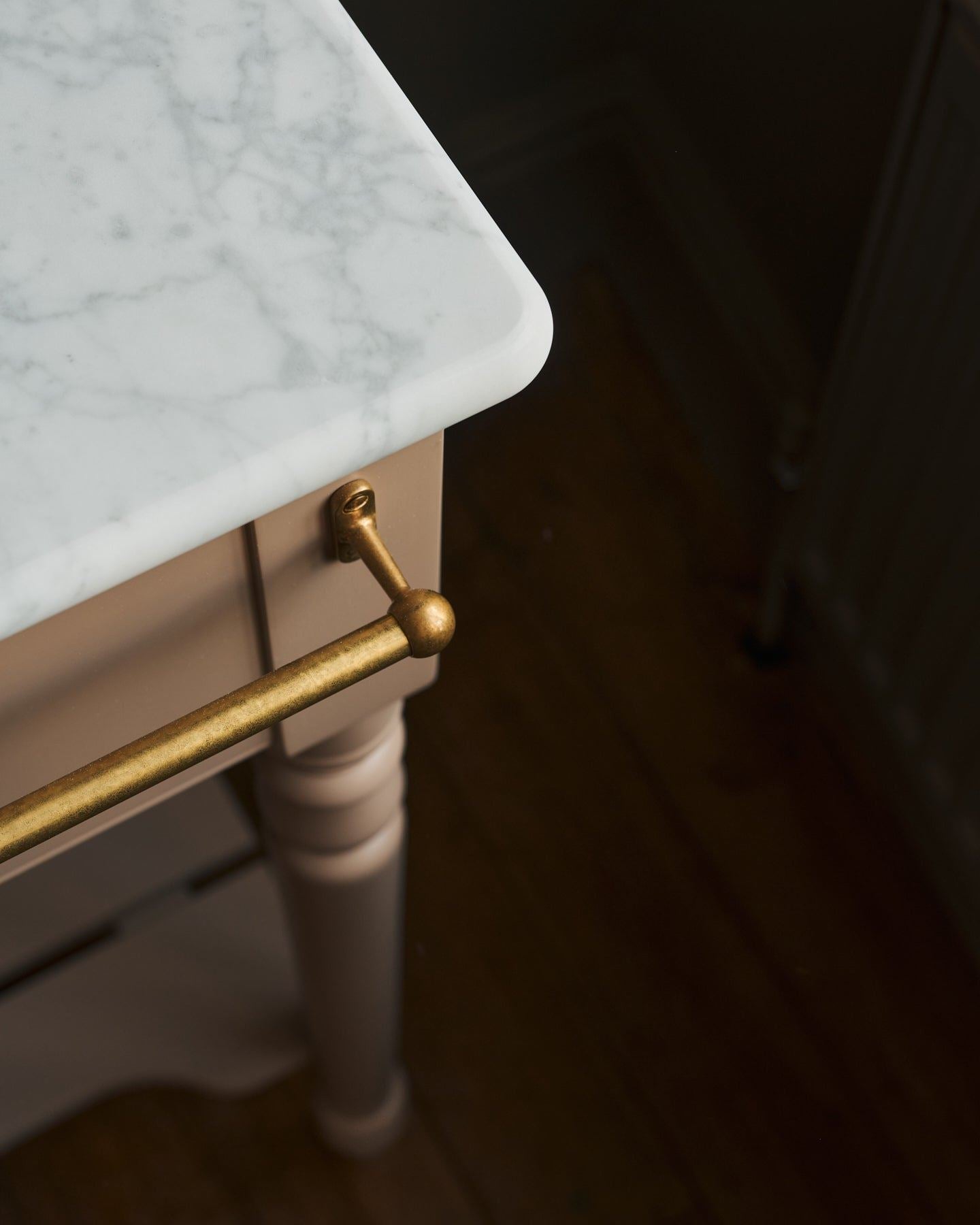A detailed view of an aged brass towel rail attached to the front of a Victorian-inspired washstand.