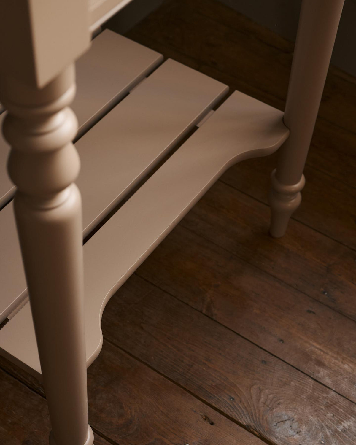 A close-up view of a pink painted slatted shelf at the base of a Victorian-inspired washstand. TEST