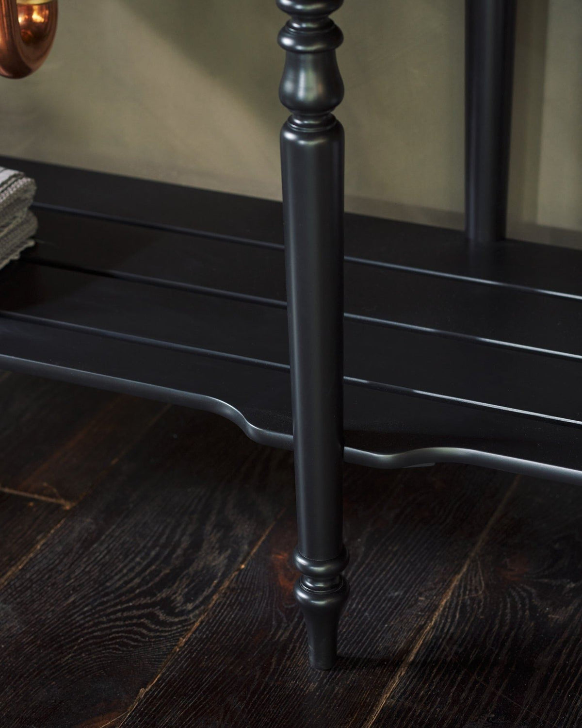 A close-up view of a black painted slatted shelf at the base of a Victorian-inspired washstand. TEST