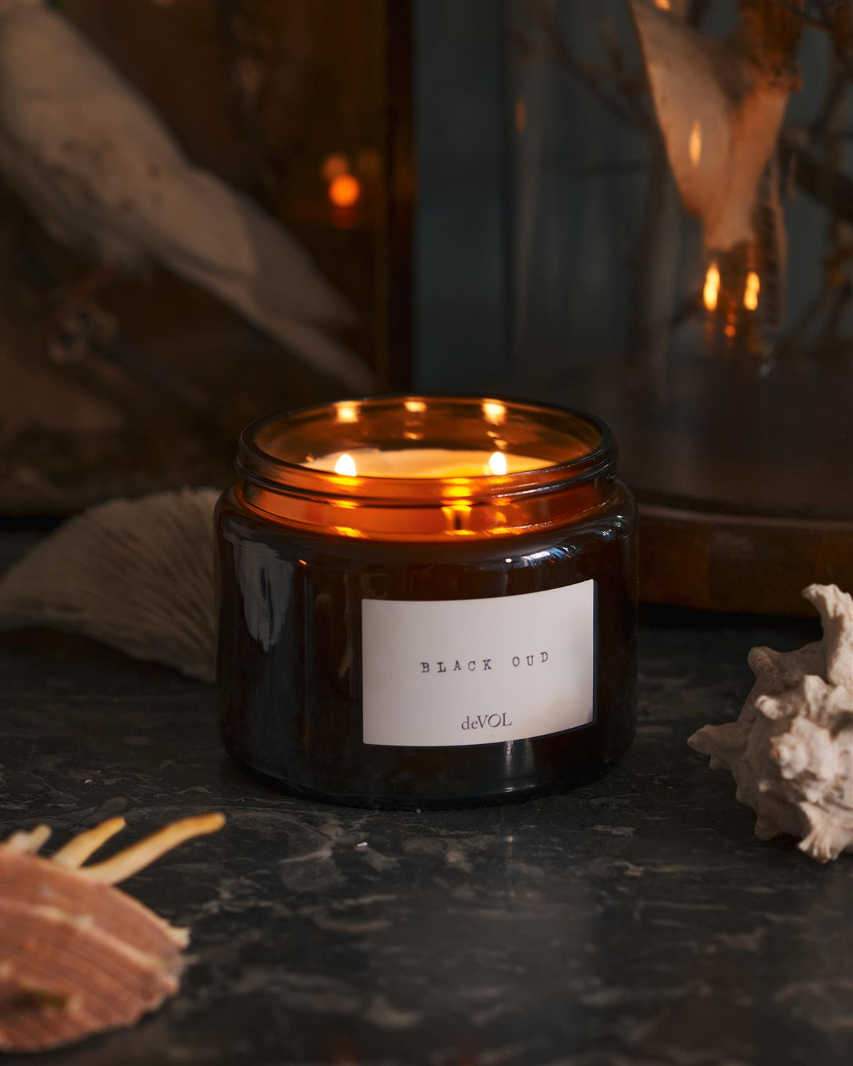 A lit large scented candle in a brown glass jar with three wicks, on a polished quartz worktop. TEST