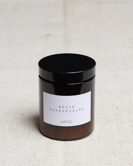 A medium scented candle in a brown glass jar with a black lid, the label reads 'Amber & Tonka Bean, deVOL'.