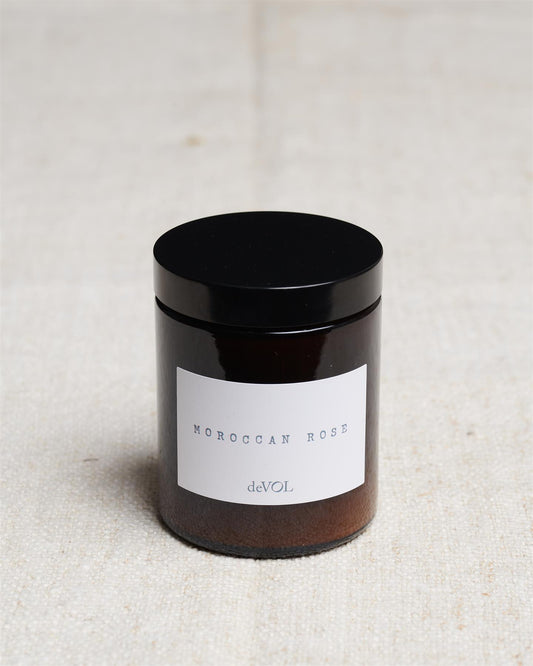 A medium scented candle in a brown glass jar with a black lid, the label reads 'Amber & Tonka Bean, deVOL'.