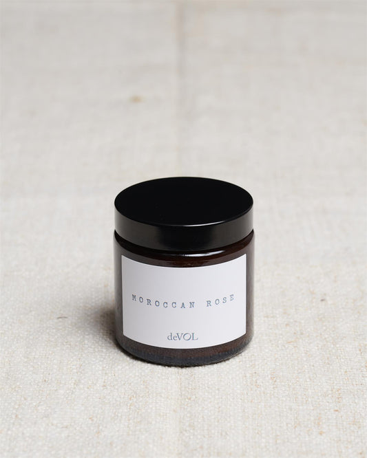 A small scented candle in a brown glass jar with a black lid, the label reads 'Amber & Tonka Bean, deVOL'.