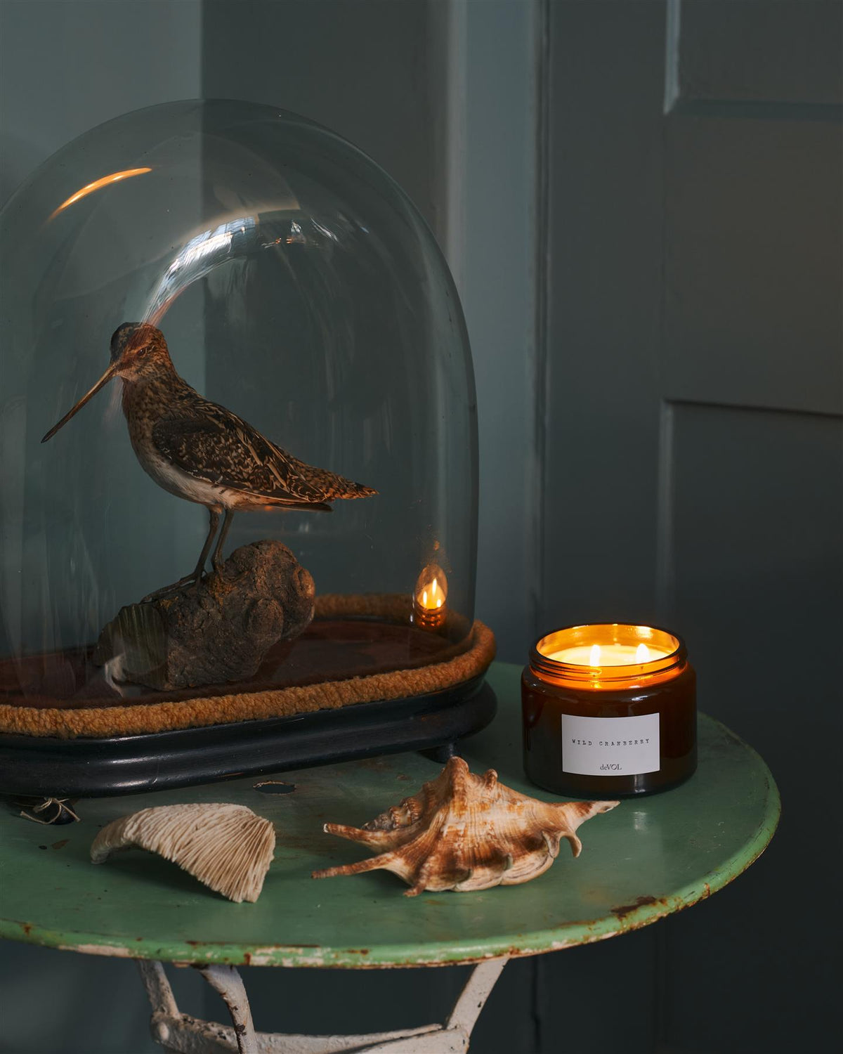 A collection of three lit scented candles in brown glass jars on a polished quartz worktop; small, medium and large. TEST