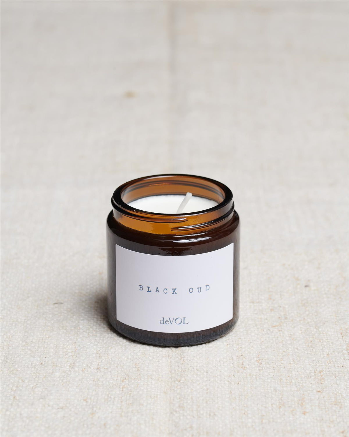 A collection of three lit scented candles in brown glass jars on a polished quartz worktop; small, medium and large. TEST