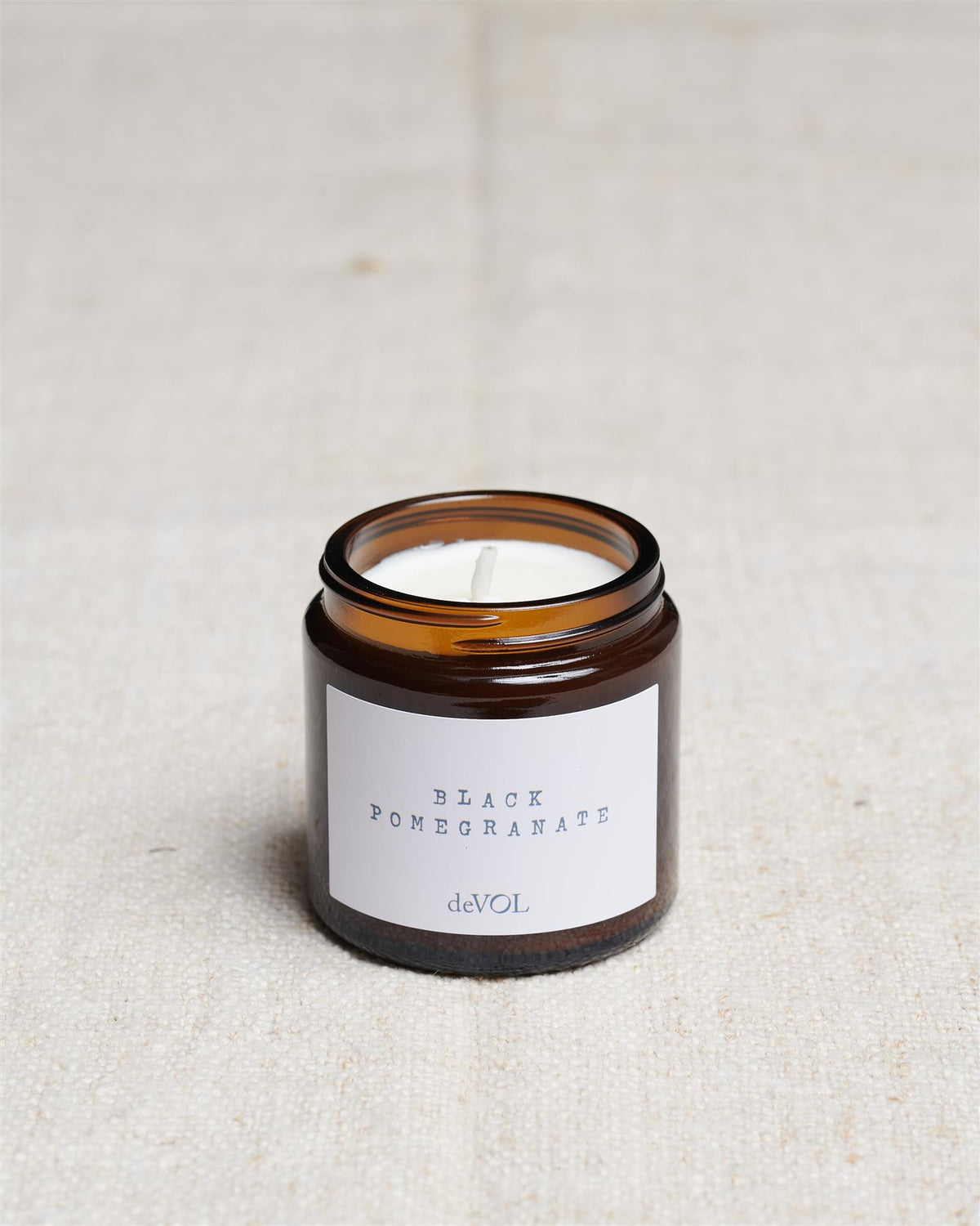 A collection of three lit scented candles in brown glass jars on a polished quartz worktop; small, medium and large. TEST
