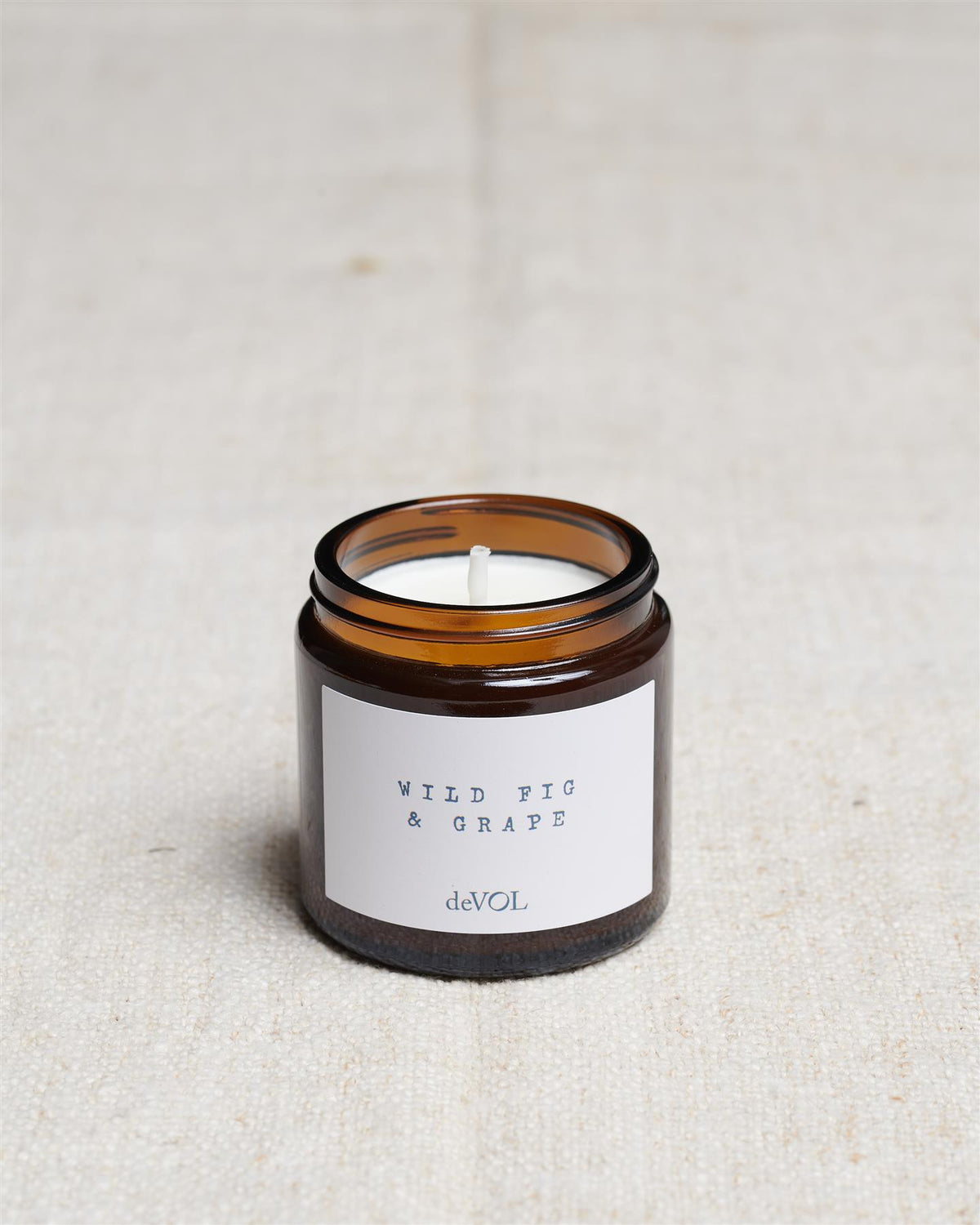 A collection of three lit scented candles in brown glass jars on a polished quartz worktop; small, medium and large. TEST