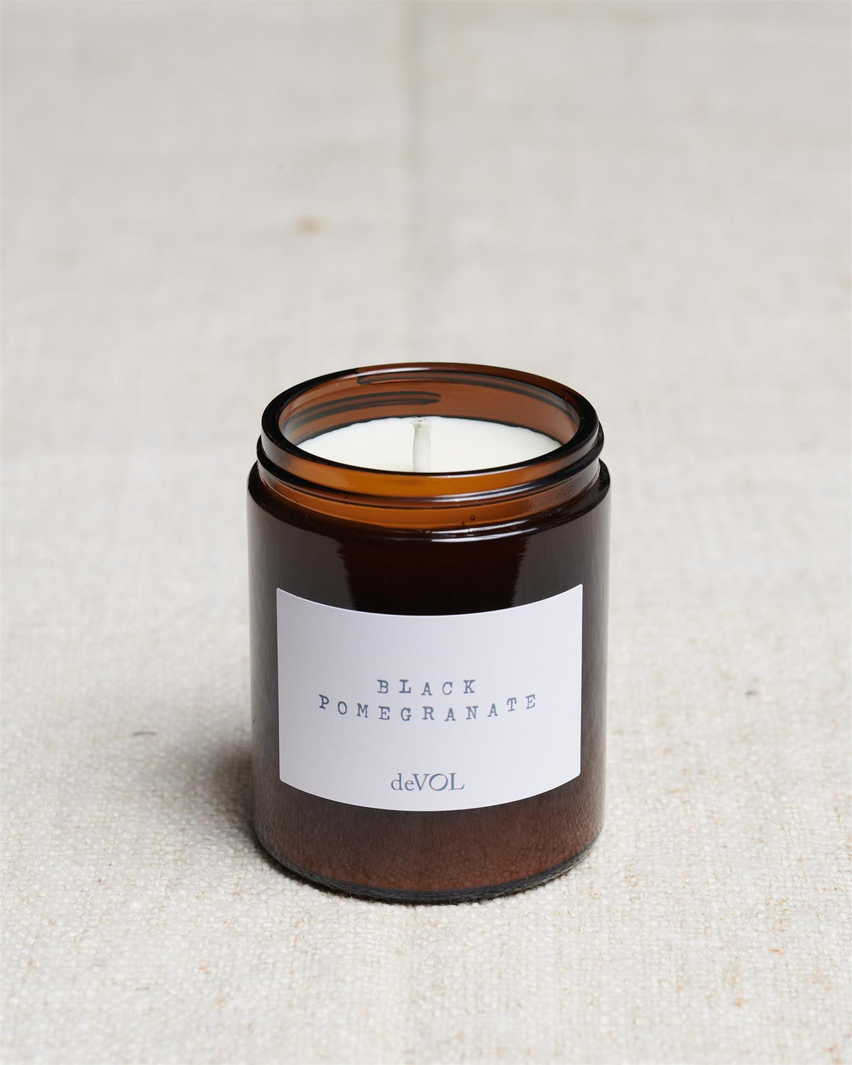 A collection of three lit scented candles in brown glass jars on a polished quartz worktop; small, medium and large. TEST