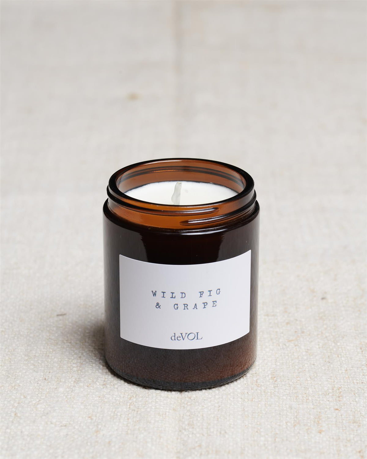 A collection of three lit scented candles in brown glass jars on a polished quartz worktop; small, medium and large. TEST