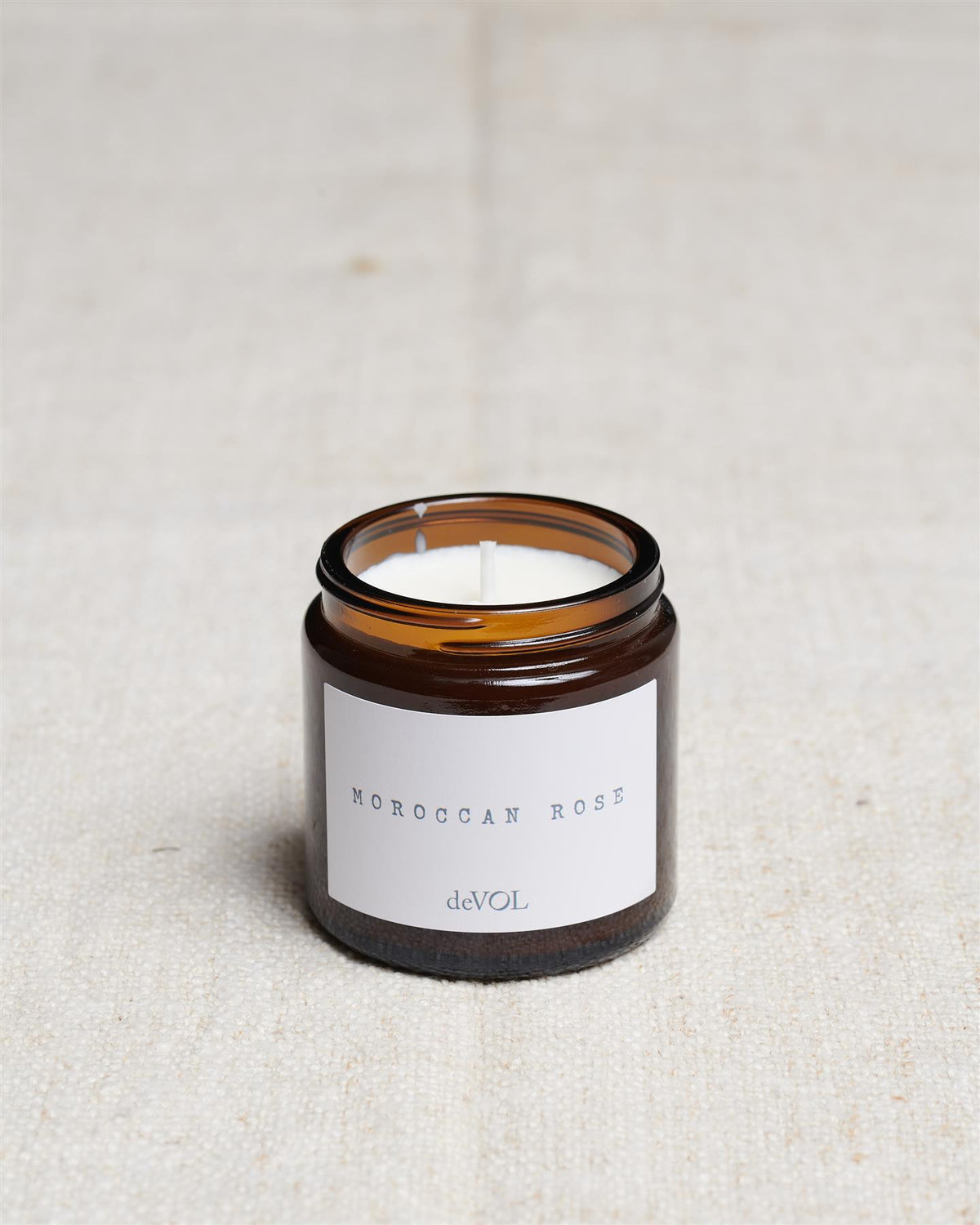 A collection of three lit scented candles in brown glass jars on a polished quartz worktop; small, medium and large. TEST