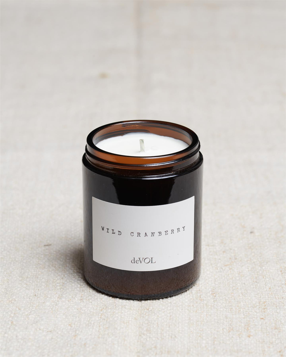 A collection of three lit scented candles in brown glass jars on a polished quartz worktop; small, medium and large. TEST