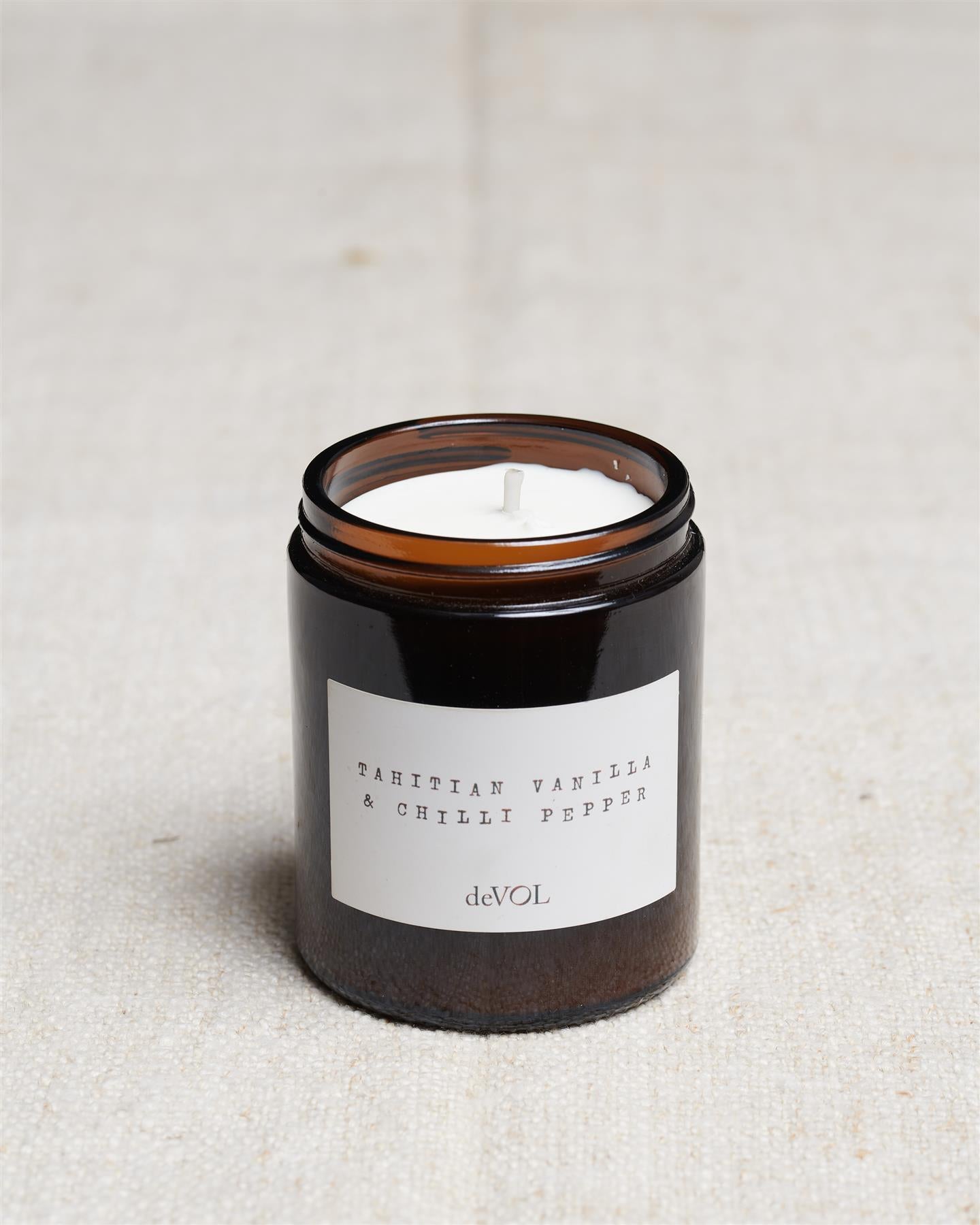 A collection of three lit scented candles in brown glass jars on a polished quartz worktop; small, medium and large.
