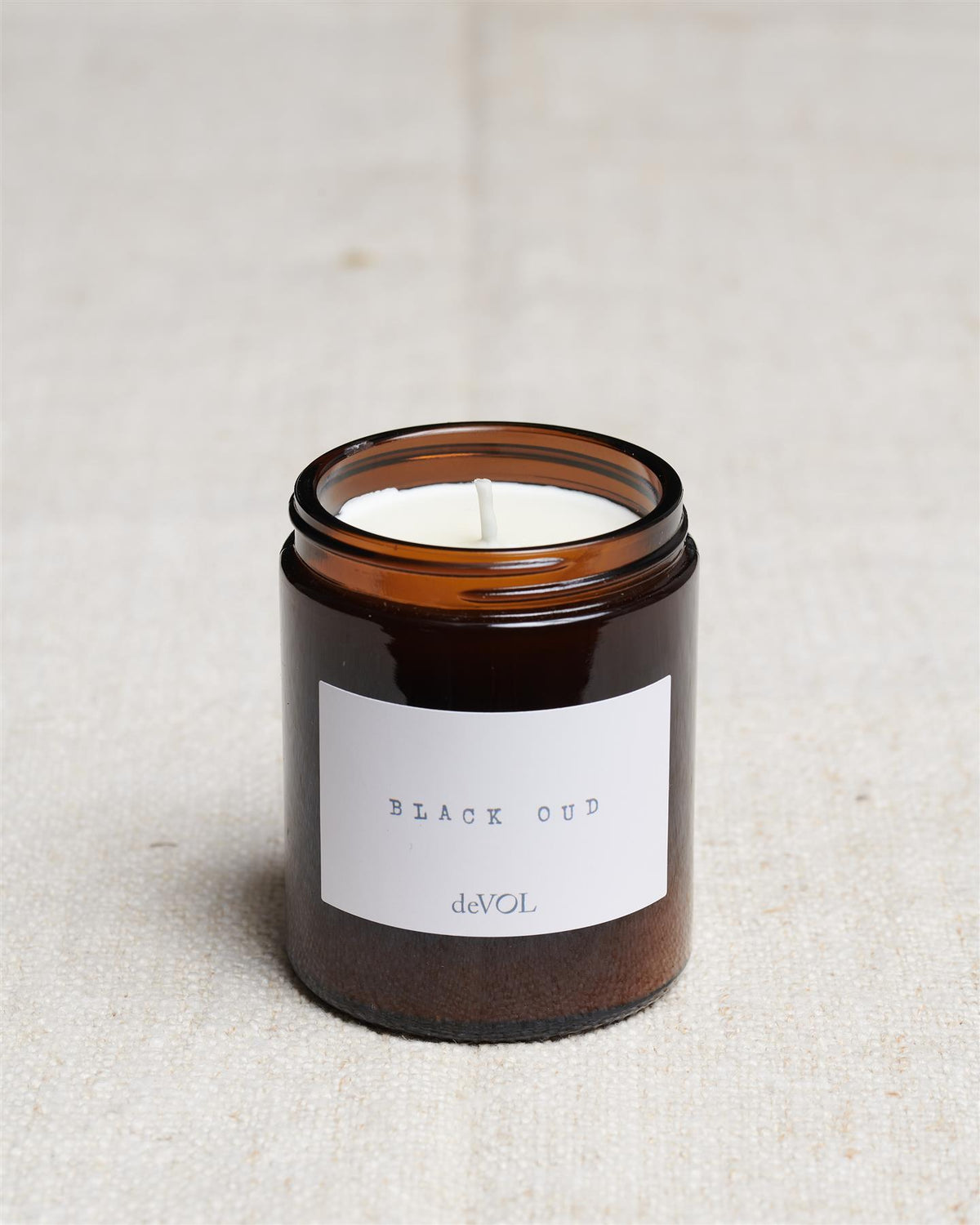 A collection of three lit scented candles in brown glass jars on a polished quartz worktop; small, medium and large. TEST