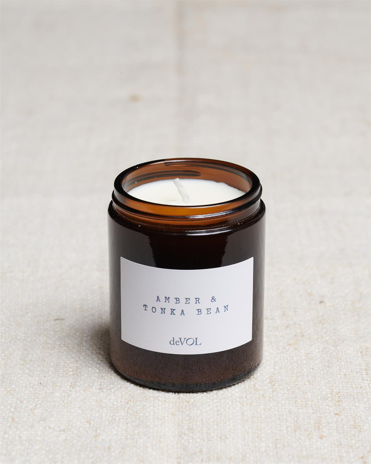 A collection of three lit scented candles in brown glass jars on a polished quartz worktop; small, medium and large. TEST