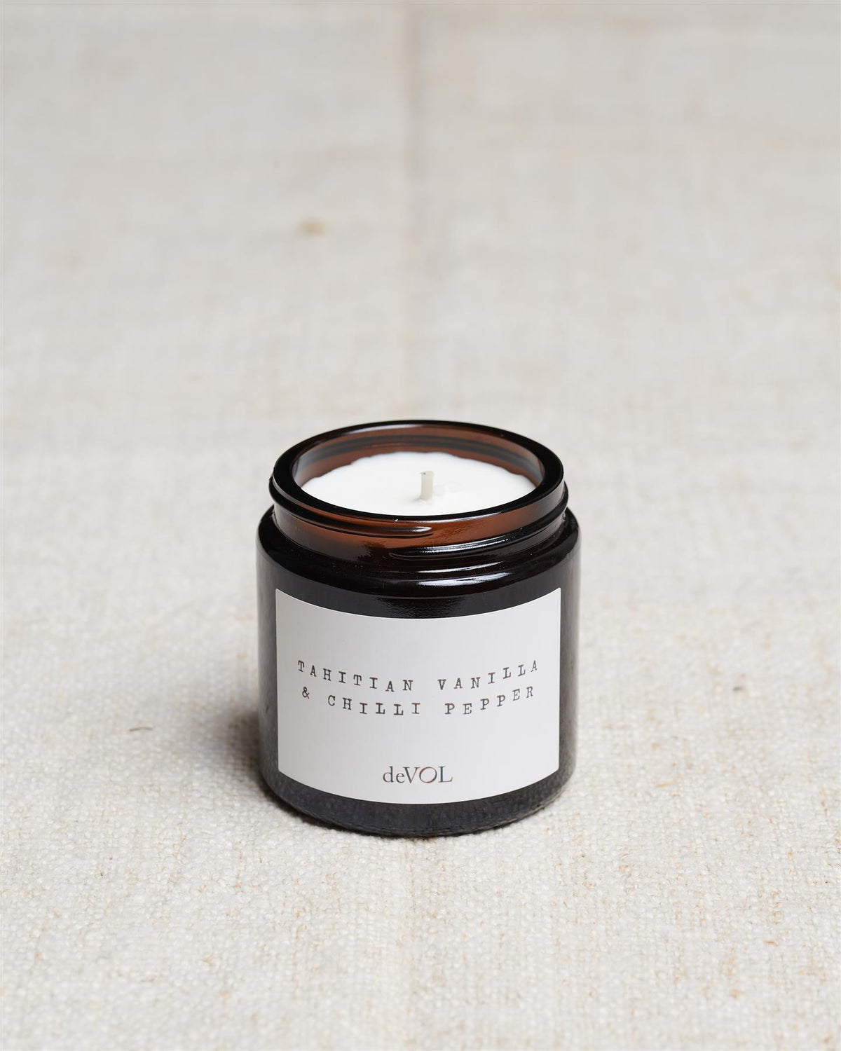 A collection of three lit scented candles in brown glass jars on a polished quartz worktop; small, medium and large. TEST