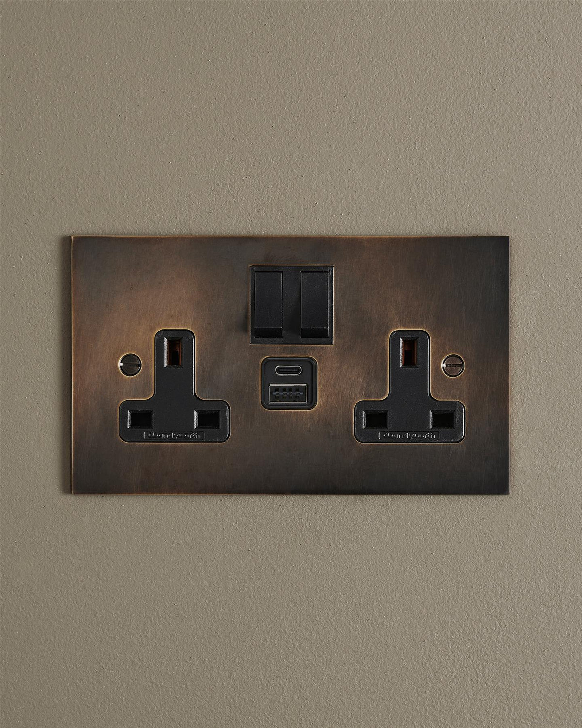 An Oxidised Brass Twin Plug Socket with USB A/C ports on a beige wall. TEST