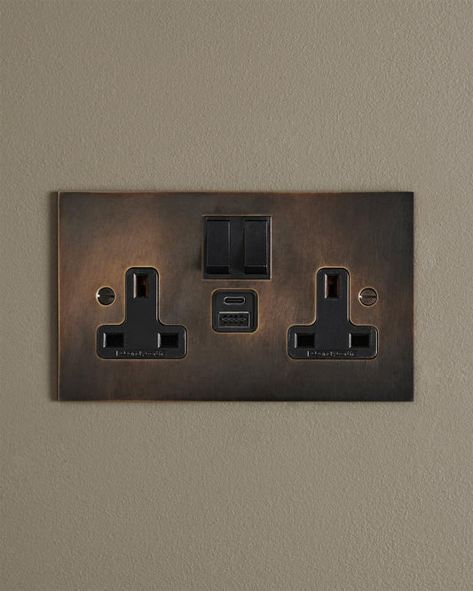 An Oxidised Brass Twin Plug Socket with USB A/C ports on a beige wall.