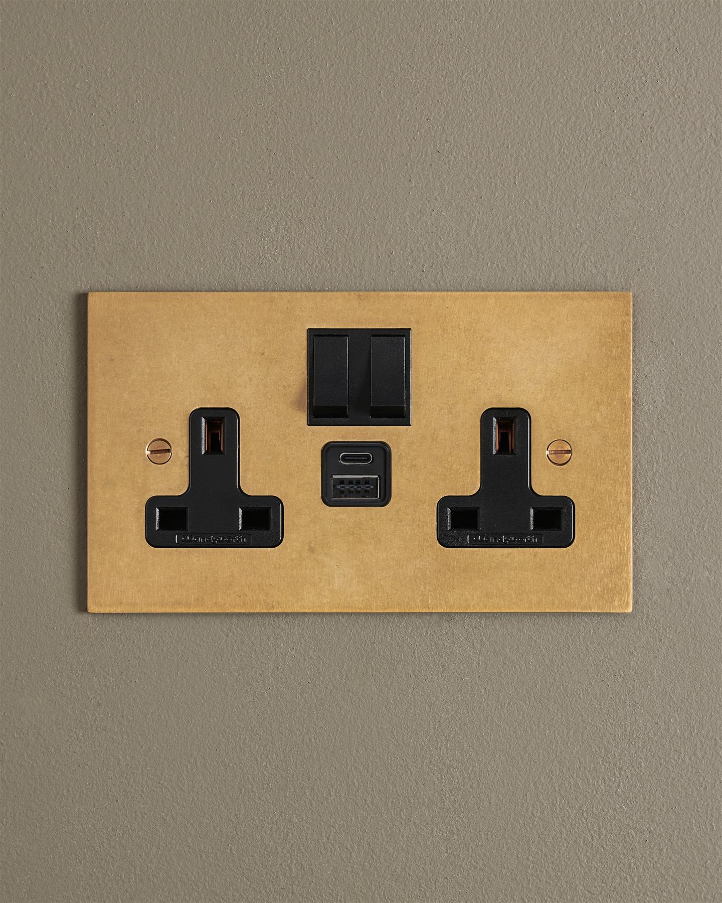 An Aged Brass Twin Plug Socket with USB A/C ports on a beige wall.