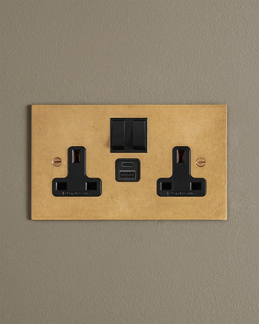 An Aged Brass Twin Plug Socket with USB A/C ports on a beige wall.