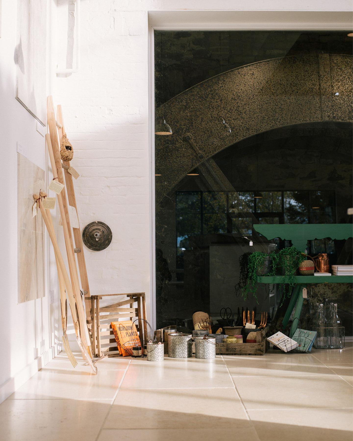 A straight-on shot looking towards the back of deVOL's flooring showroom. Light pours in through the huge glazed windows, casting pools of light and shadows on the wooden staircase and Light Jerusalem Limestone flooring.