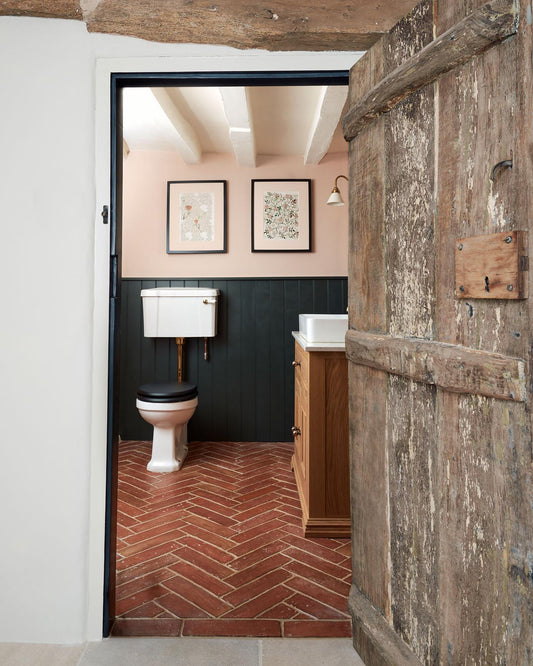 A small toilet with traditional styling, dark blue painted tongue and groove panelling, soft pink walls, an oak vanity unit and parquet terracotta flooring with an authentic aged finish.