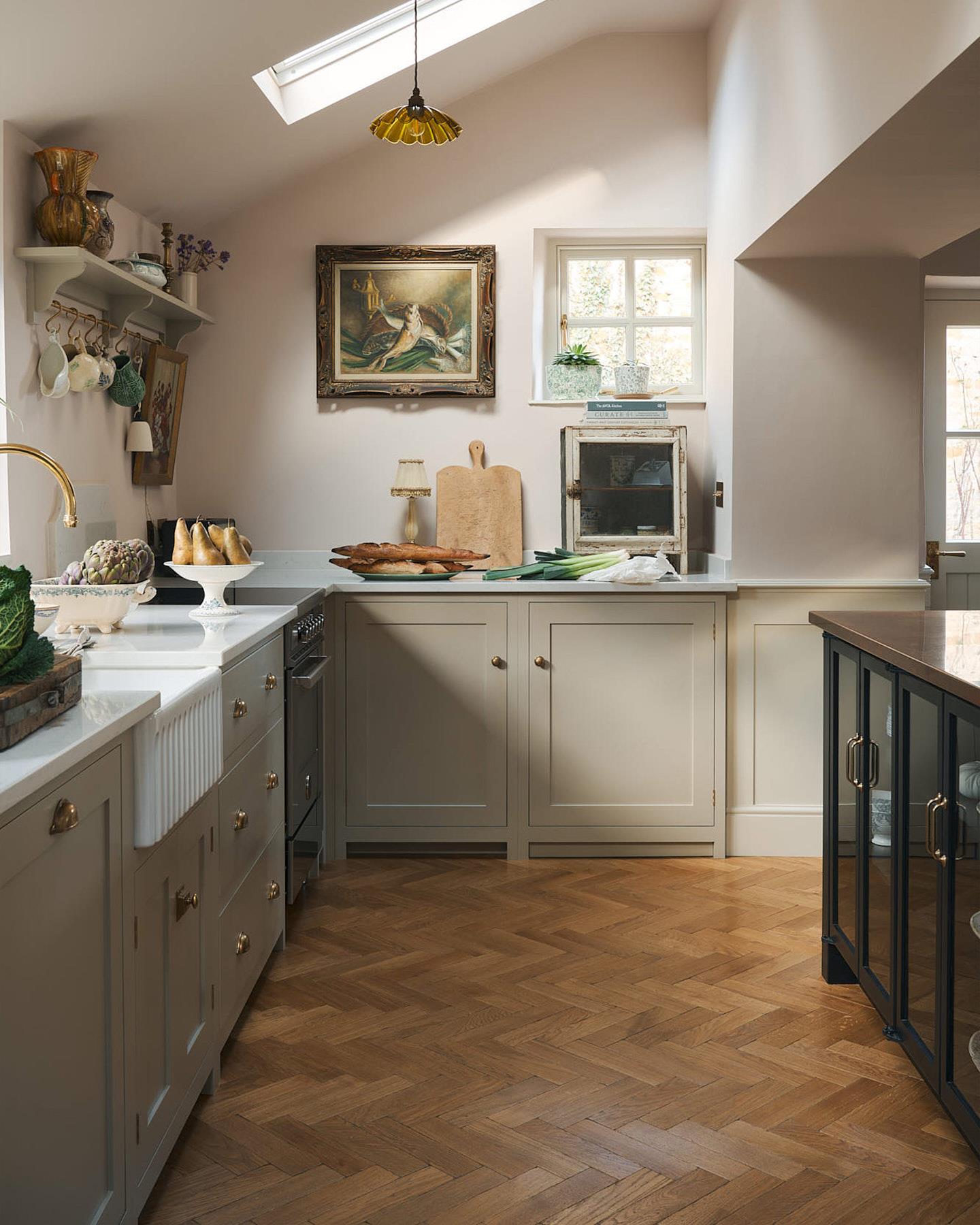 A straight-on view of a minimal room with white walls, a marble fireplace surround, fitted white painted Shaker-style cabinetry and oak parquet flooring with a warm aged finish.