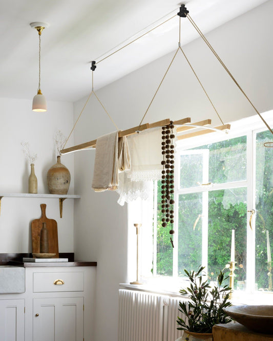 An oblique view of a laundry maid with wooden slats and aluminium brackets, hanging from the ceiling in a Mediterranean-inspired room with white walls, terracotta flooring and rustic styling.