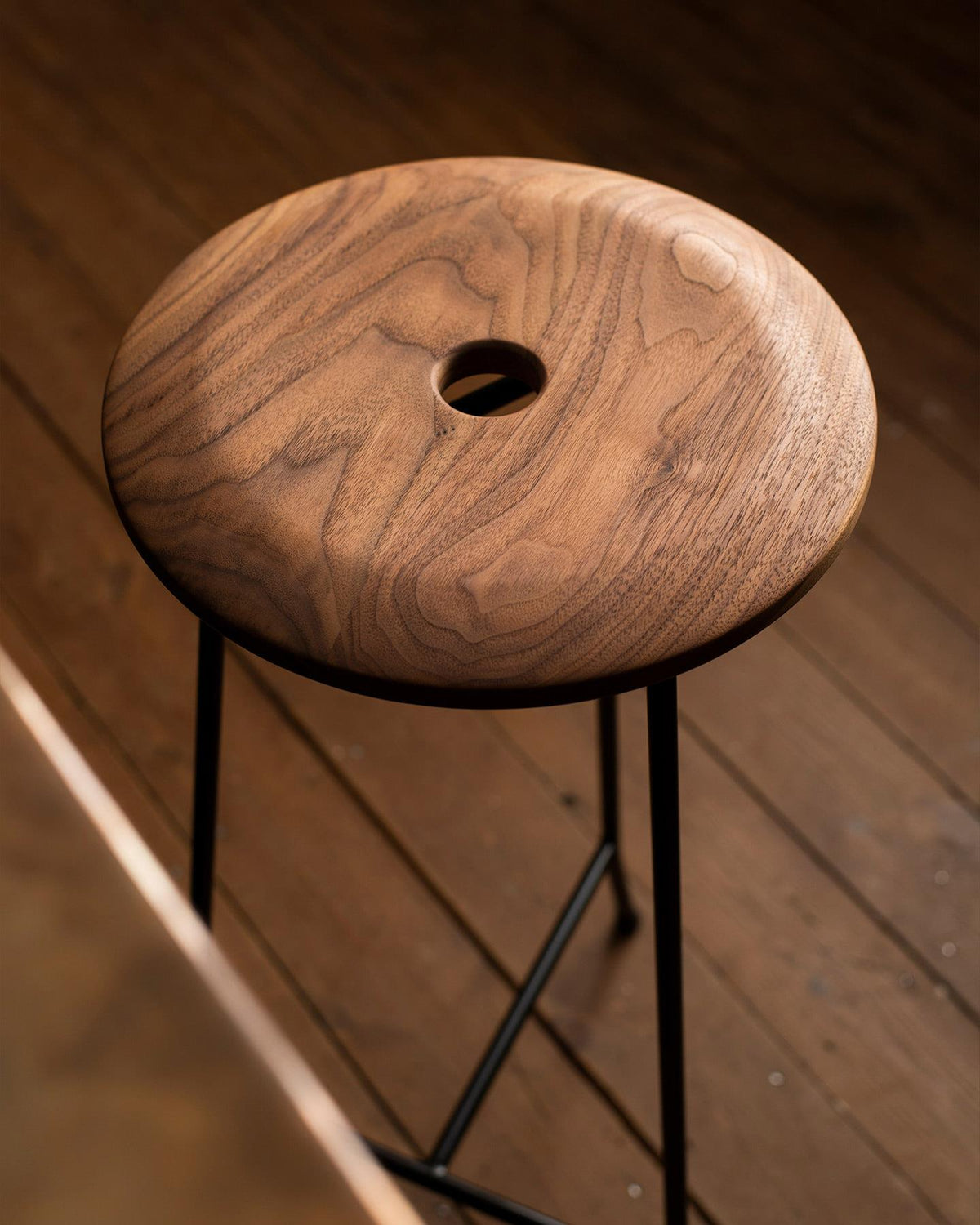 An oblique view of two round walnut seat tops with a central holes, one in a dark stained finish and the other in a natural oiled finish. TEST