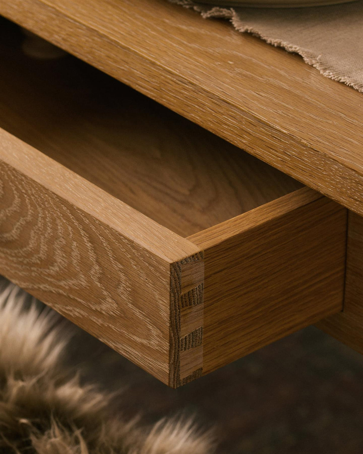 A close-up view of a shallow drawer in the apron of a Shaker-style oak dining table. TEST