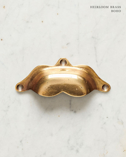 A bohemian-style cup handle for a kitchen cupboard or drawer with a warm burnished brass finish.