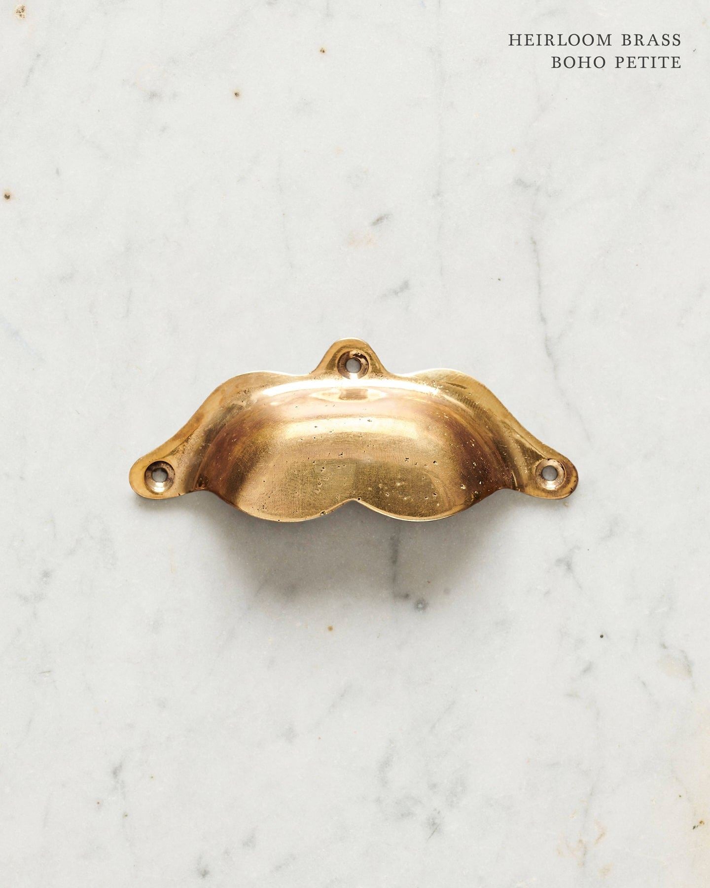 A small bohemian-style cup handle for a kitchen cupboard or drawer with a warm burnished brass finish.