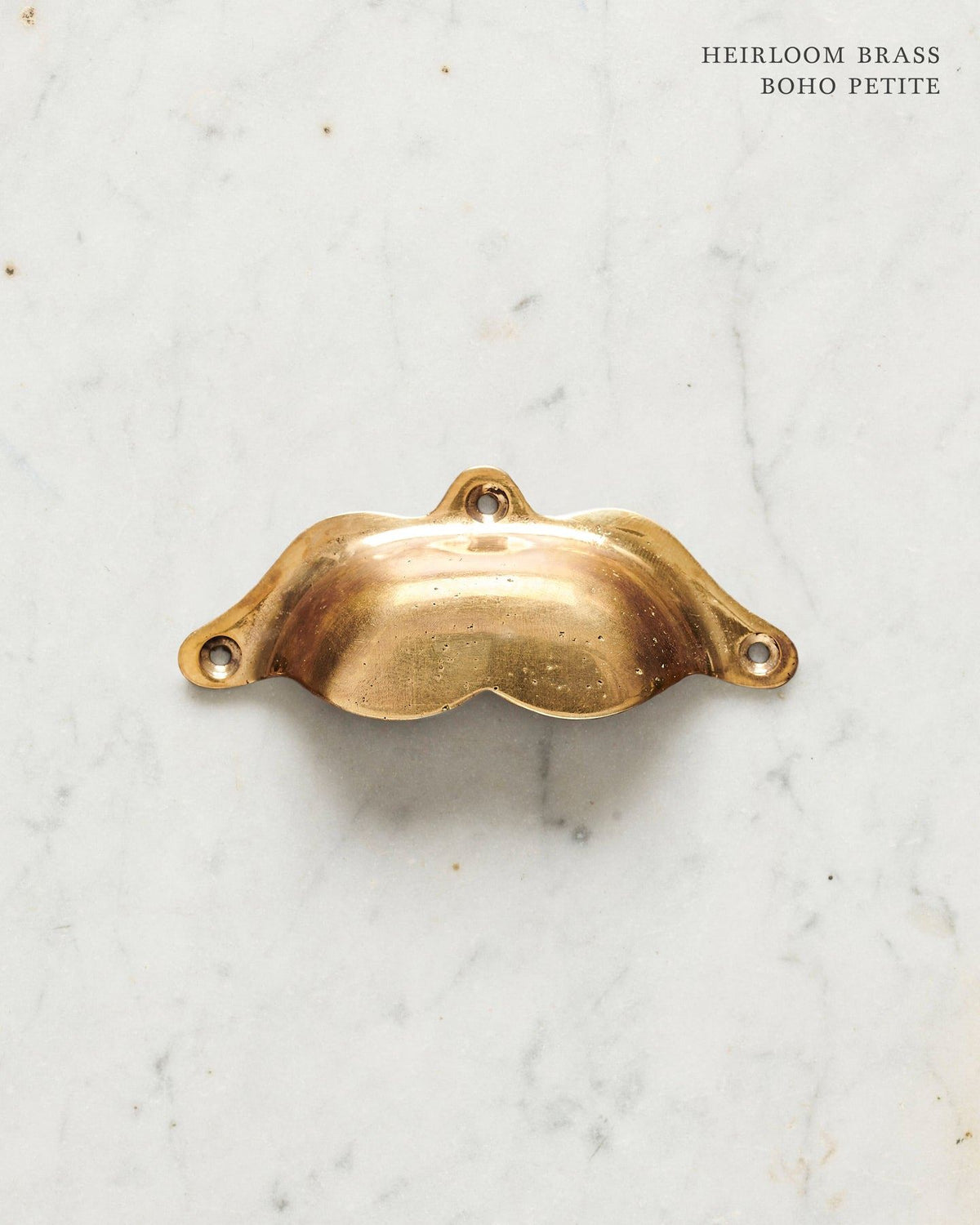 A small bohemian-style cup handle for a kitchen cupboard or drawer with a warm burnished brass finish. TEST